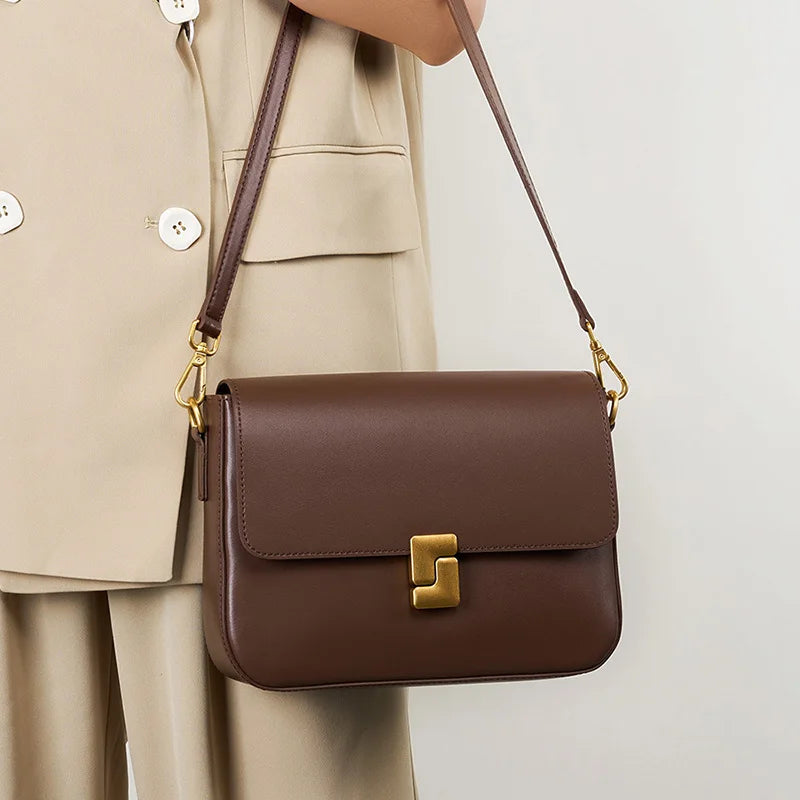 Sac à Main en Cuir Femme à bandoulière Marron, avec une boucle de fermeture dorée, porté par une femme dans une tenue beige, sur un fond gris.