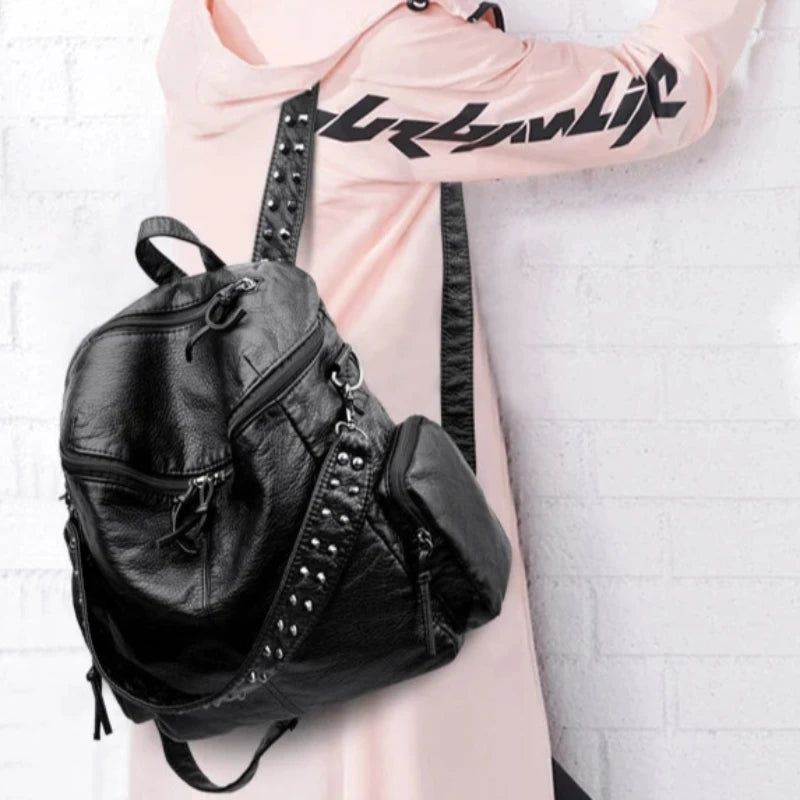 Sac à Main et à Dos Femme Tendance en Simili, de couleur noire, avec décorations à rivets sur les bretelles, porté par une personne avec un haut rose.