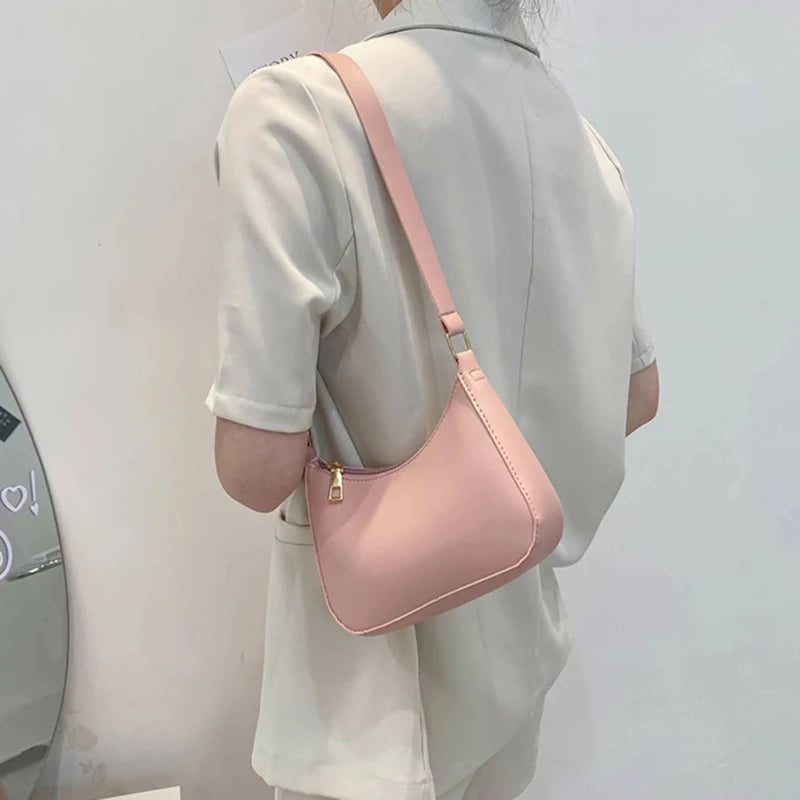 Sac à Main Baguette Simili Rose Rétro, avec bandoulière, porté sur l'épaule d'une femme de dos, habillée en blanc.