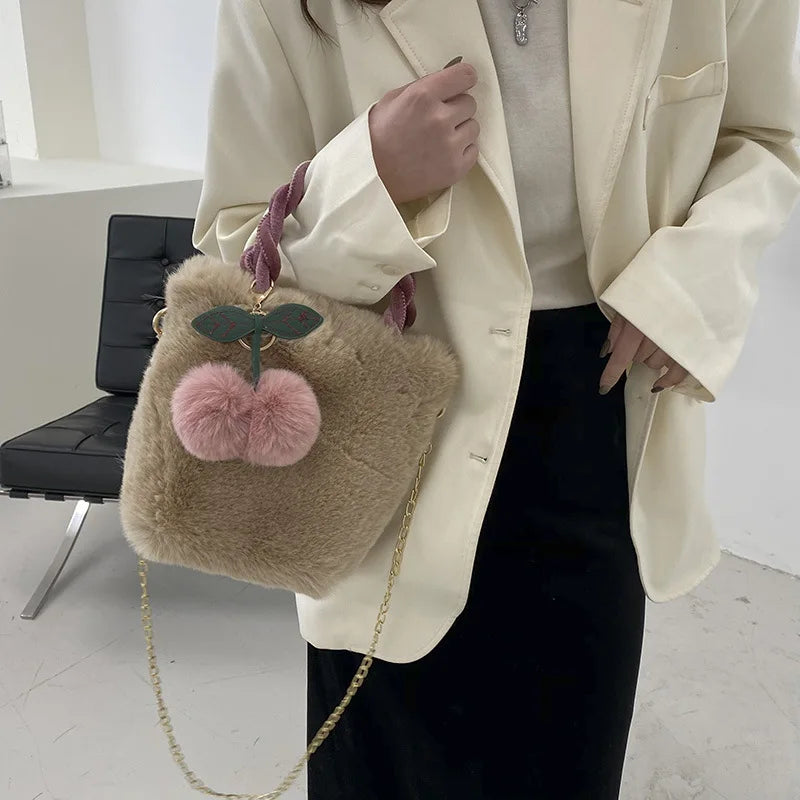 Sac à Main Fausse Fourrure avec Pendentif Cerise, avec une chaînette dorée pour un port en bandoulière, et de couleur marron, porté sur le bras d'une femme avec une veste blanche.