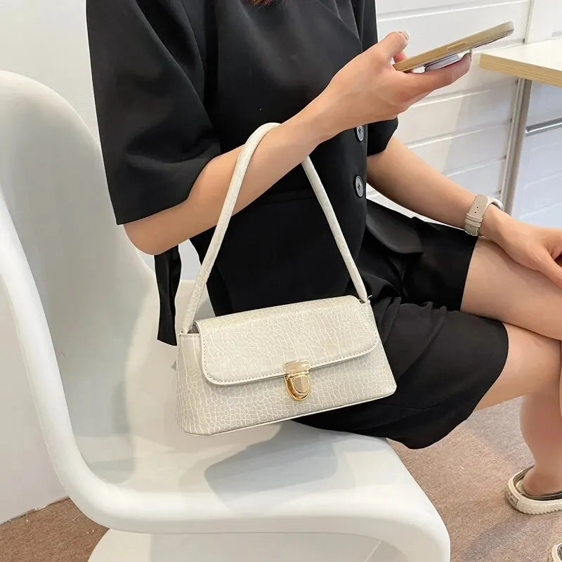 Sac à Main Baguette Simili Blanc Élégant, petit format, avec une fermeture dorée, porté par une femme habillée en noir assise sur une chaise.