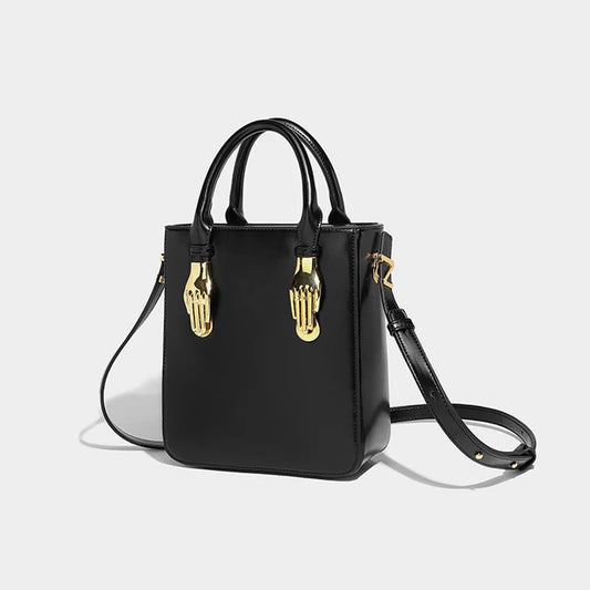 Sac à Main Panier Noir Original et Élégant, forme de mains dorées sur le sac, sur un fond gris et blanc.